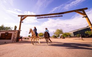 Two female riders on horseback walking under the sign at Horseshoe Park and Equestrian Centre.