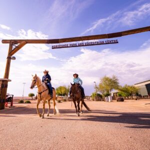 Two female riders on horseback walking under the sign at Horseshoe Park and Equestrian Centre.