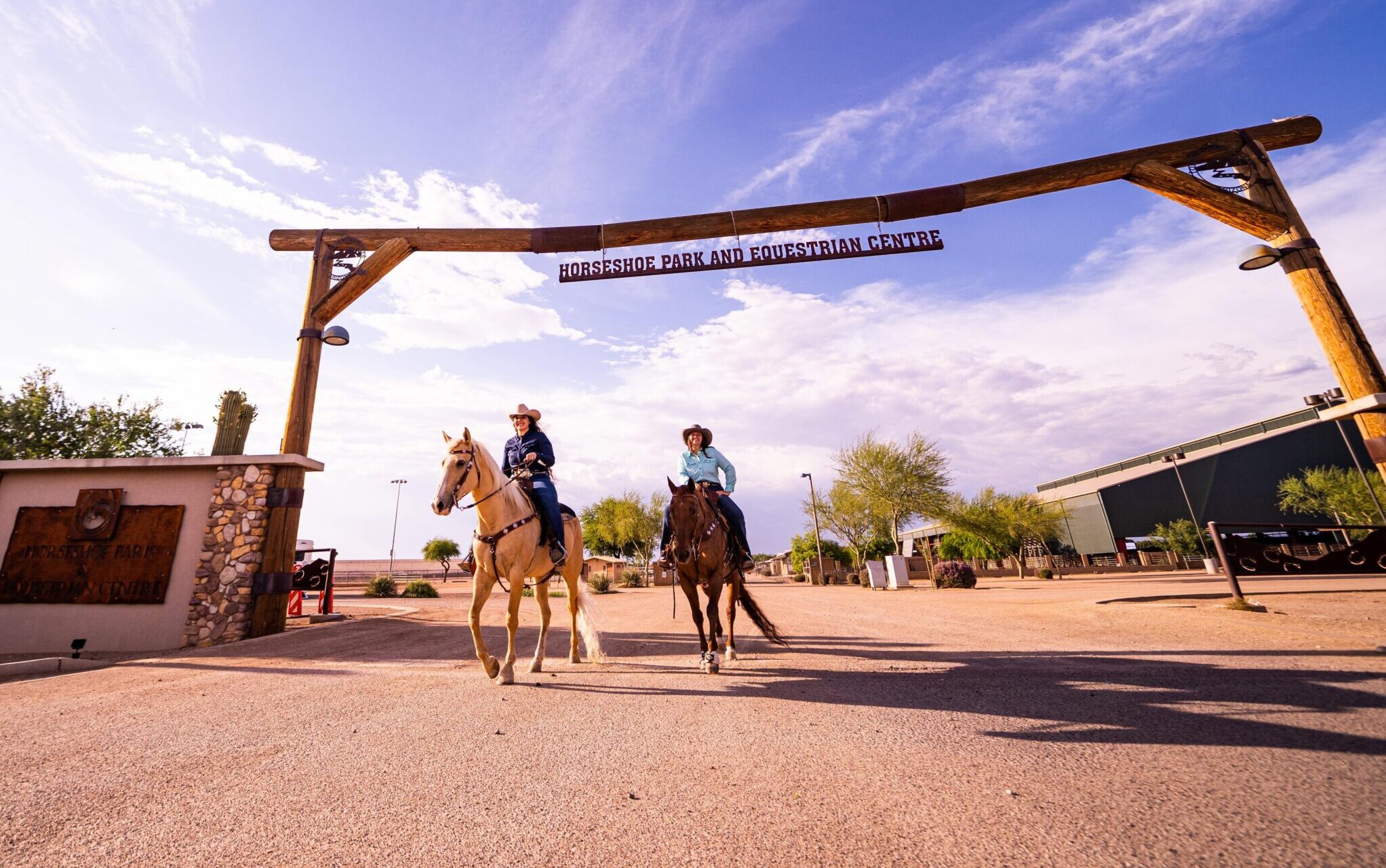 Two female riders on horseback walking under the sign at Horseshoe Park and Equestrian Centre.