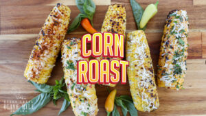 Corn Roast text header with four pieces of roasted corn on a cutting board.